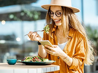 Woman smiling while looking at her phone and eating