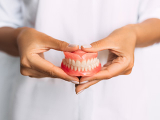 Woman in white holding complete set of dentures in front of abdomen