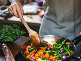 Someone in gray apron sauteing vegetables