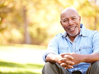 Man in denim jacket sitting and smiling outside