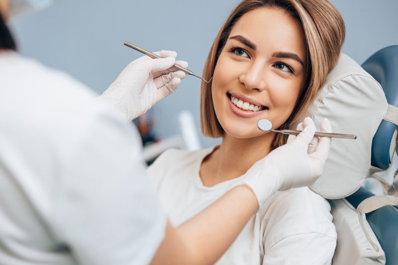 A young female patient smiling while her dentist prepares to administer a regular checkup