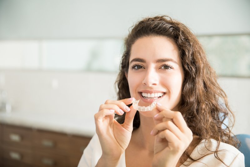 a young woman prepares to insert a clear retainer after Invisalign treatment