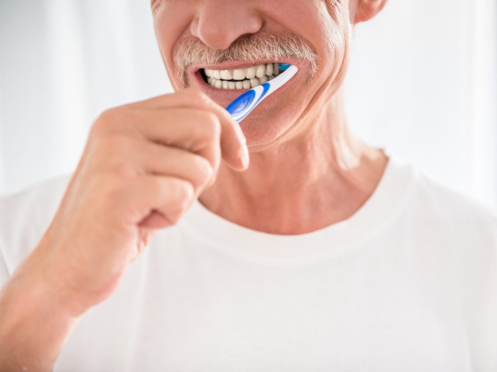 Closeup of senior man in white shirt brushing his teeth